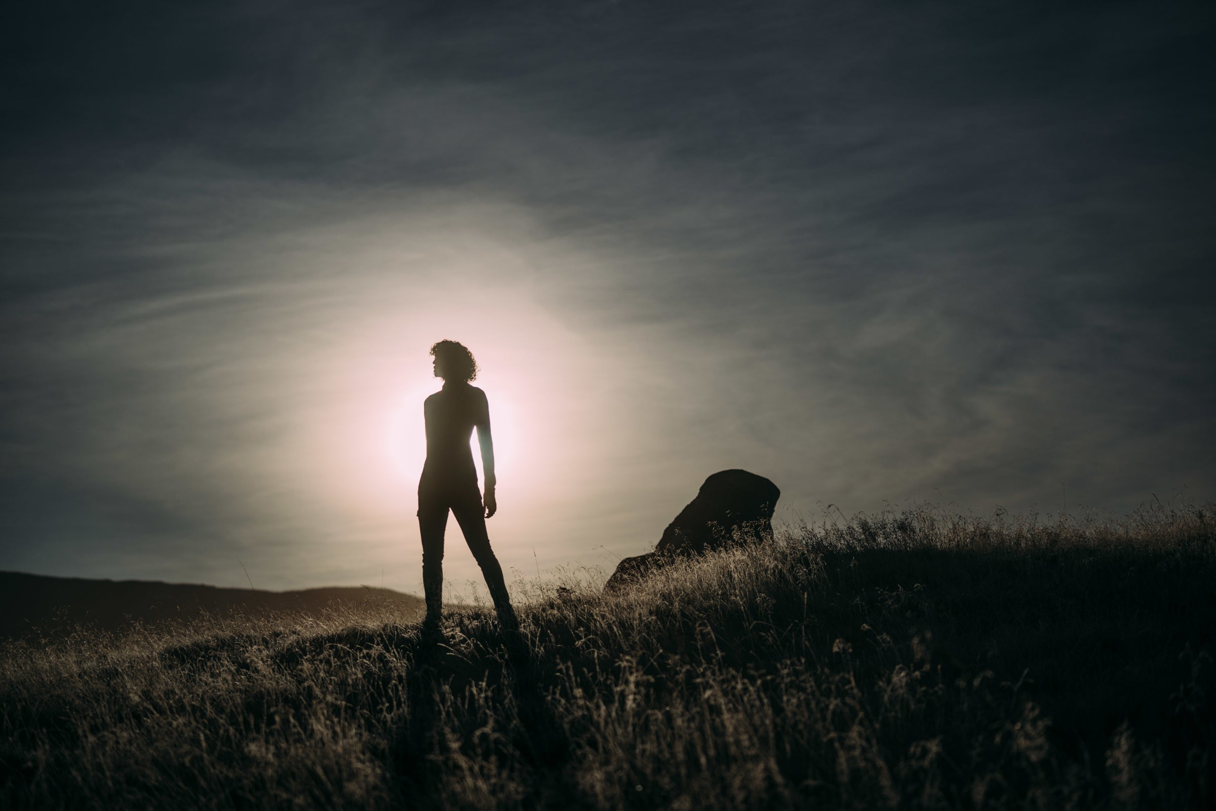 Silhouette d’une personne debout au sommet d’une colline, découpée devant le soleil couchant sous un ciel dégagé.