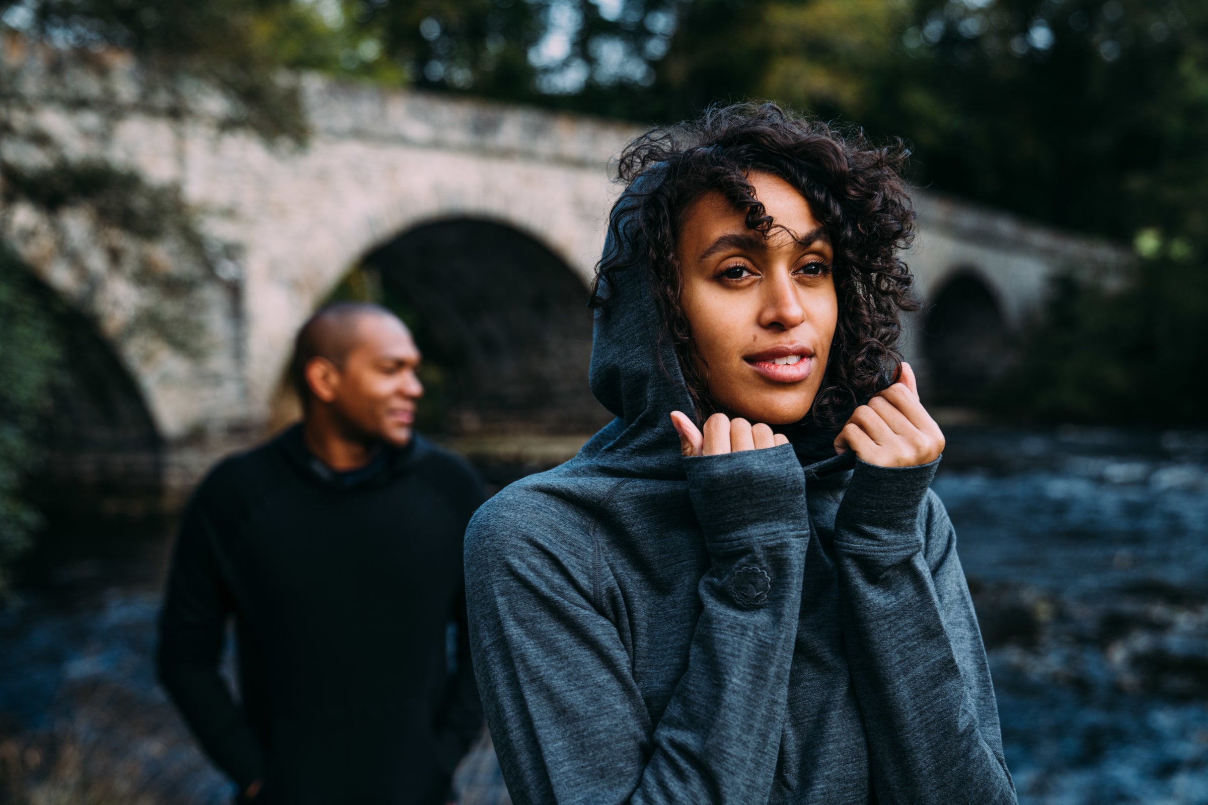 Une femme portant un hoodie en laine Merino près d’une rivière, souriante et détendue