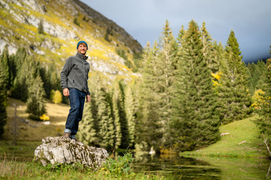 Man standing on a rock in a mountain forest, wearing outdoor gear