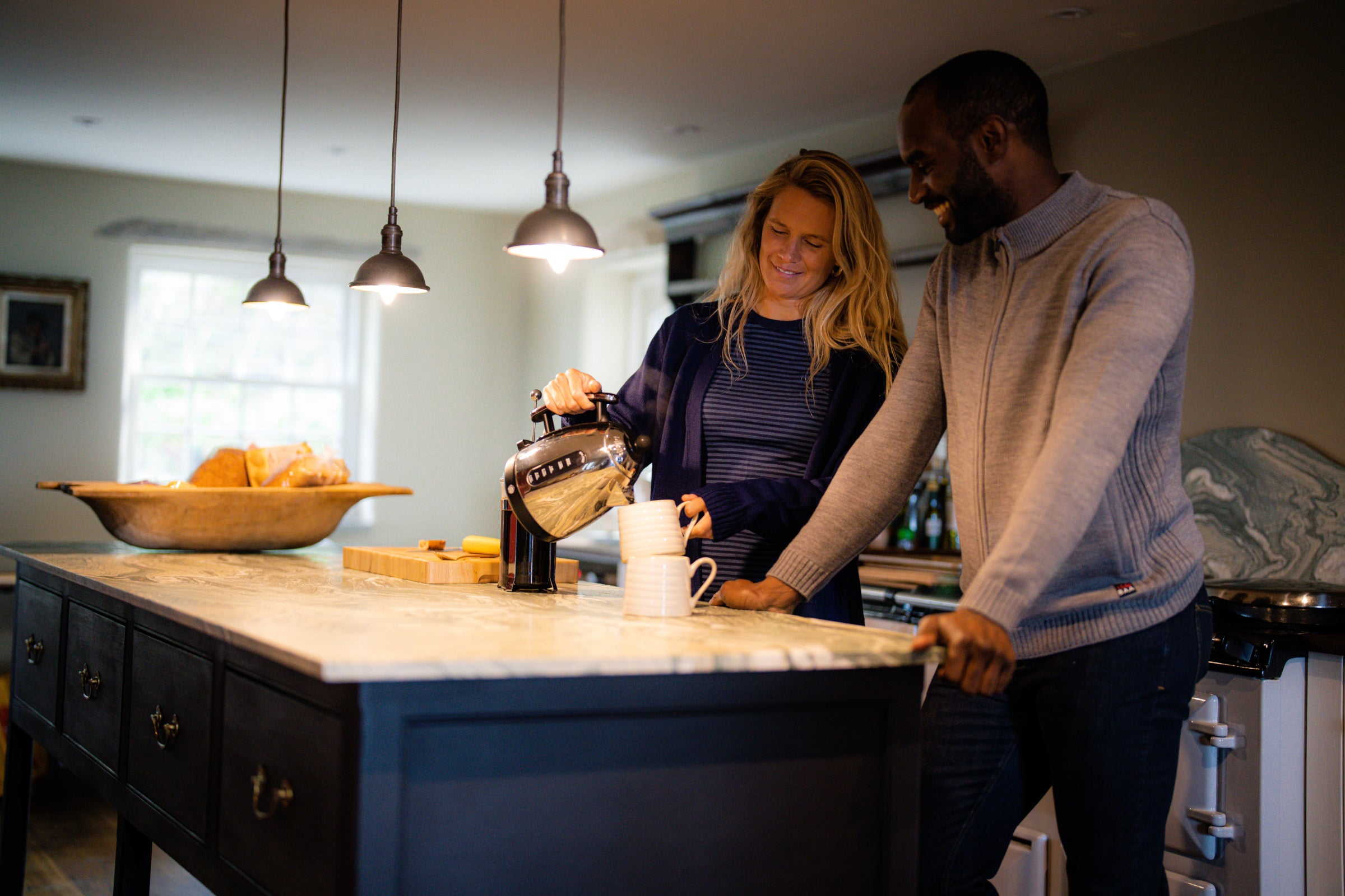Un homme et une femme dans une cuisine chaleureuse, partageant un moment pendant que la femme sert du thé